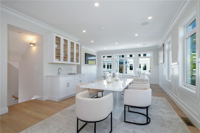 dining space with light hardwood / wood-style floors, indoor wet bar, and ornamental molding