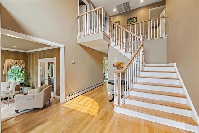 stairway with a high ceiling, baseboard heating, and wood-type flooring