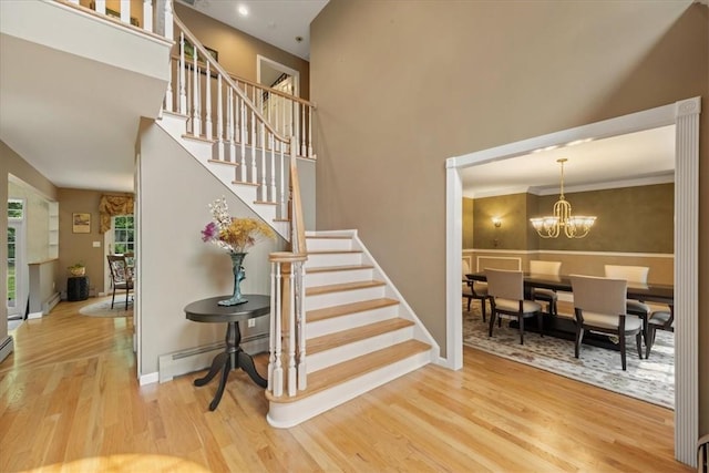 stairs with hardwood / wood-style flooring, an inviting chandelier, ornamental molding, and a baseboard heating unit