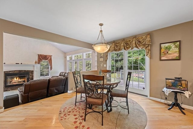 dining space featuring a high end fireplace, light wood-type flooring, and lofted ceiling