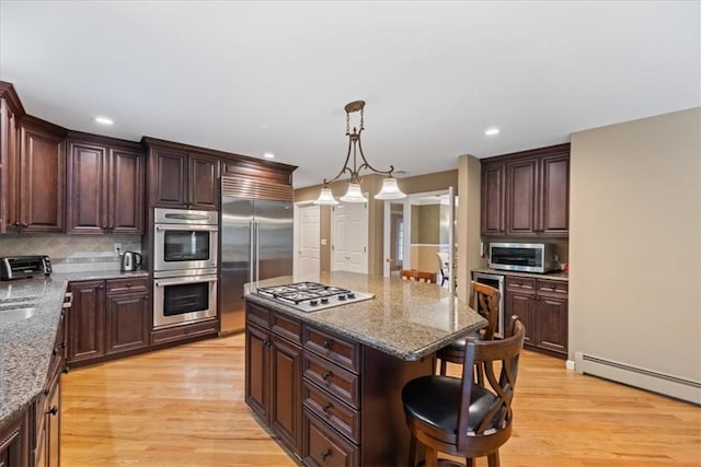 kitchen featuring a breakfast bar area, light hardwood / wood-style flooring, hanging light fixtures, and appliances with stainless steel finishes