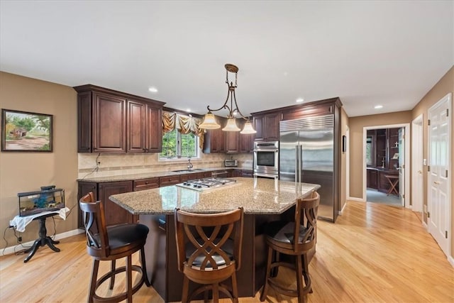 kitchen featuring light stone countertops, a kitchen island, light wood-type flooring, and appliances with stainless steel finishes