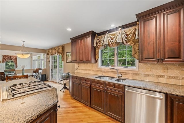 kitchen featuring appliances with stainless steel finishes, light wood-type flooring, tasteful backsplash, sink, and hanging light fixtures