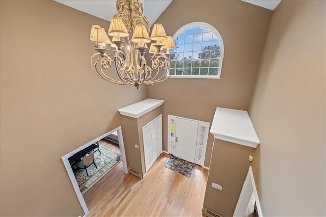 foyer with a chandelier, light wood-type flooring, vaulted ceiling, and a baseboard heating unit