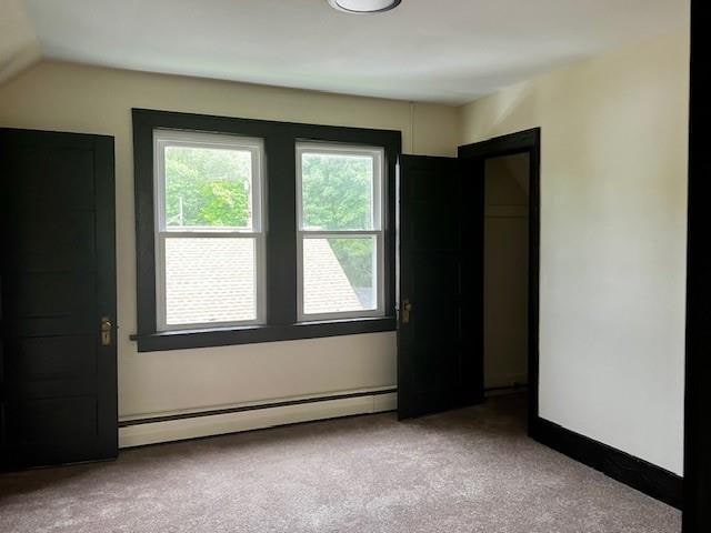 unfurnished room with vaulted ceiling, light colored carpet, and a baseboard heating unit