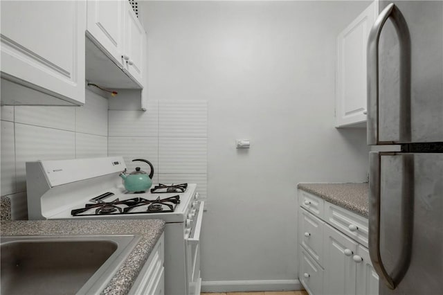 kitchen with tasteful backsplash, stainless steel fridge, white cabinets, and white range with gas stovetop