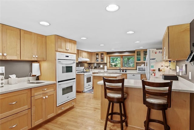 kitchen featuring a kitchen bar, white appliances, sink, and light wood-type flooring