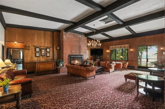 living room with a brick fireplace, brick wall, beam ceiling, an inviting chandelier, and carpet floors