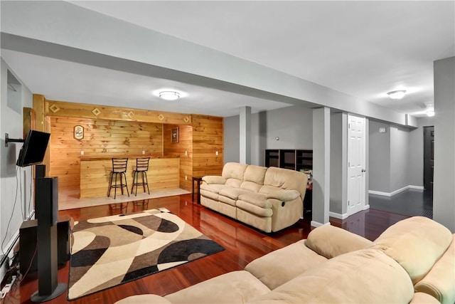 living room featuring bar area, wooden walls, and dark wood-type flooring