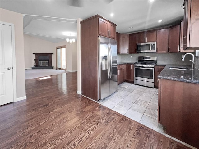 kitchen with sink, tasteful backsplash, dark stone counters, appliances with stainless steel finishes, and light wood-type flooring