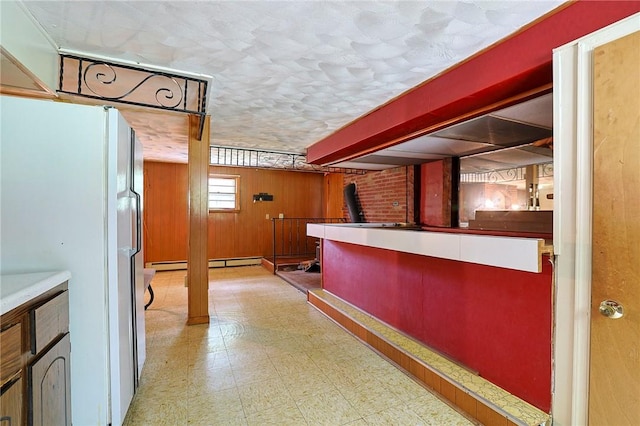 bar with baseboard heating, wooden walls, and white fridge