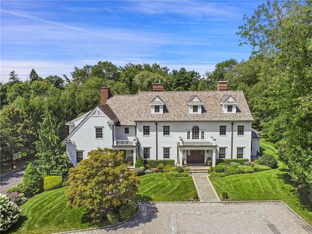 view of front of property featuring a chimney, a front lawn, and a balcony