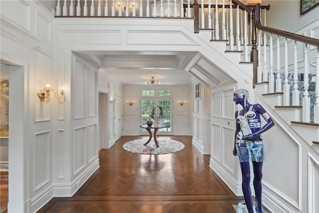 entryway featuring stairway, a chandelier, ornamental molding, and a decorative wall