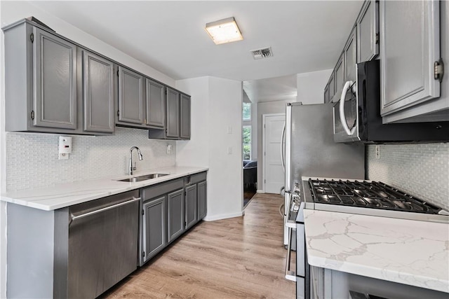 kitchen with light wood-type flooring, stainless steel appliances, gray cabinets, and backsplash