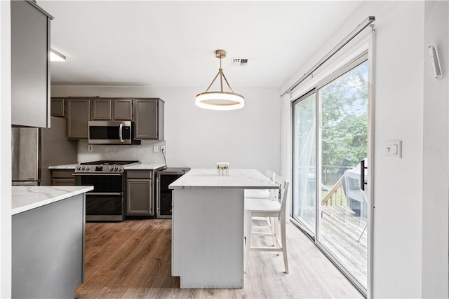 kitchen featuring decorative backsplash, stainless steel appliances, hardwood / wood-style flooring, a center island, and hanging light fixtures