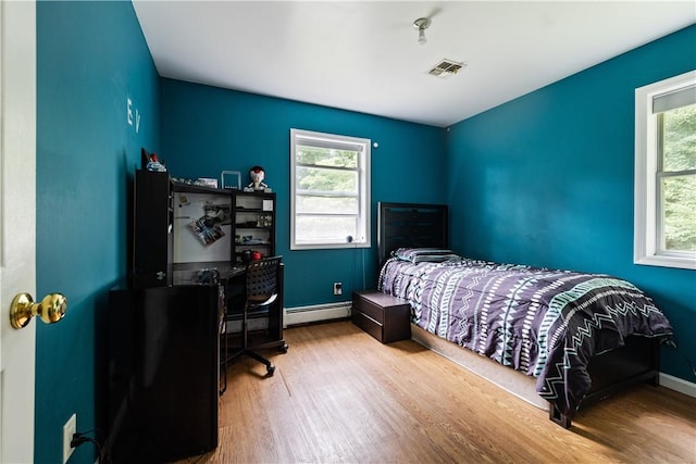 bedroom featuring baseboard heating, multiple windows, and hardwood / wood-style floors