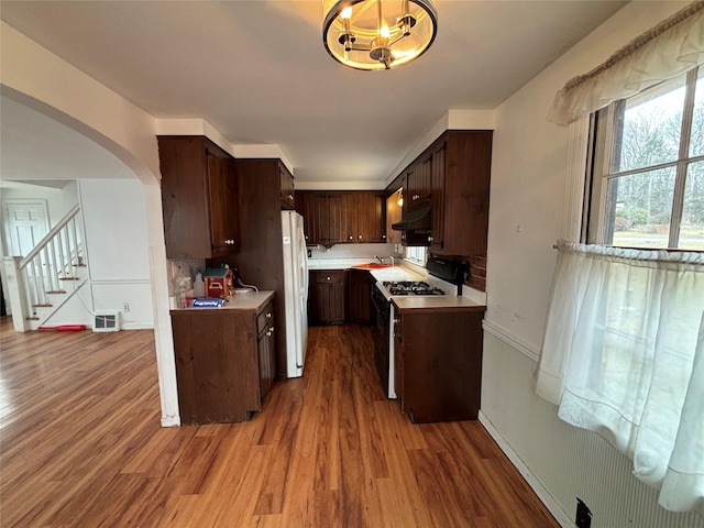 kitchen featuring hardwood / wood-style floors, white refrigerator, dark brown cabinets, black gas stove, and backsplash