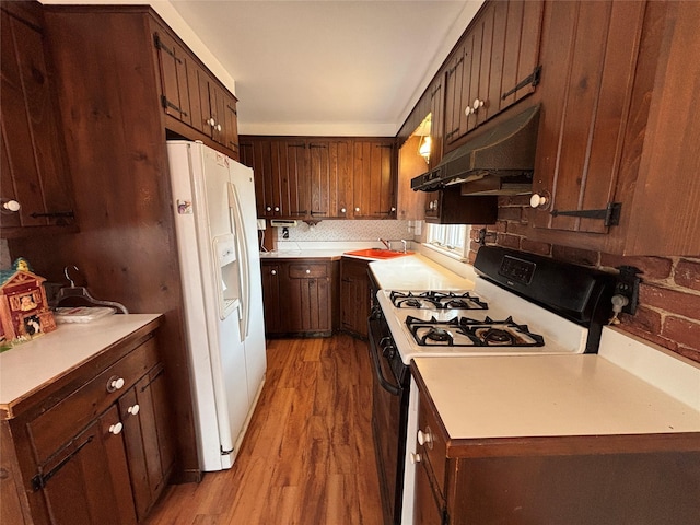 kitchen featuring white refrigerator with ice dispenser, light hardwood / wood-style flooring, tasteful backsplash, range with gas stovetop, and sink