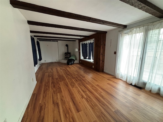 unfurnished living room featuring wood-type flooring, a wood stove, and beam ceiling