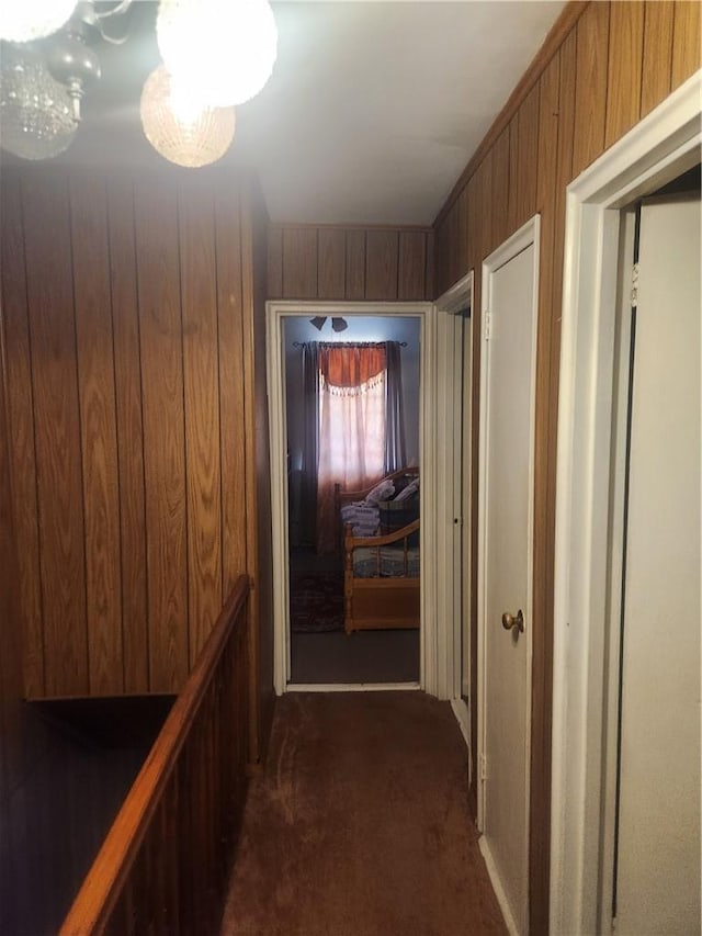 corridor with wood walls, a notable chandelier, and dark colored carpet