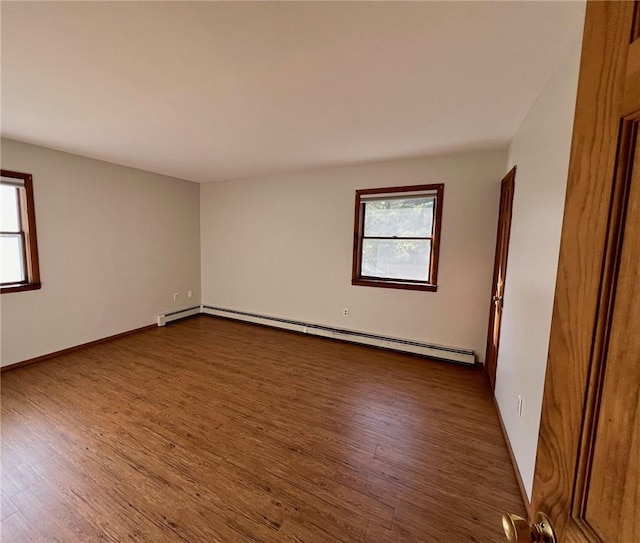 unfurnished room featuring baseboard heating, a wealth of natural light, and dark hardwood / wood-style floors