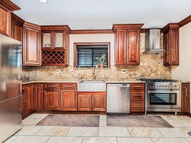 kitchen with appliances with stainless steel finishes, backsplash, light stone counters, sink, and wall chimney range hood