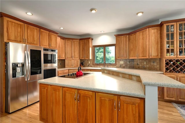 kitchen with decorative backsplash, light wood-type flooring, an island with sink, and appliances with stainless steel finishes