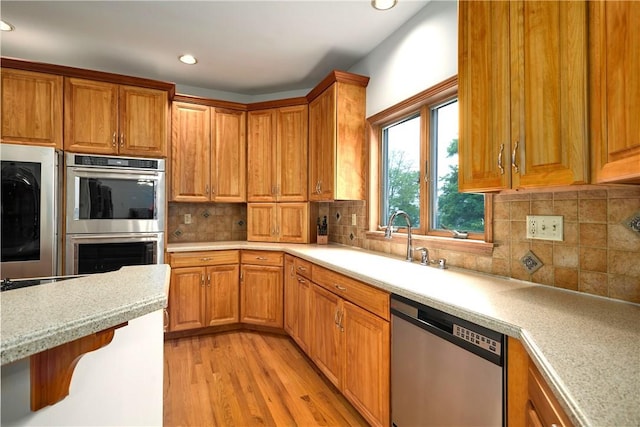 kitchen with appliances with stainless steel finishes, tasteful backsplash, a breakfast bar, sink, and light hardwood / wood-style floors