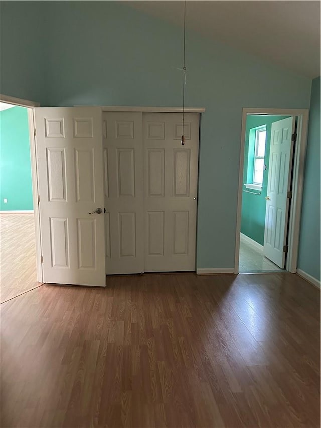 unfurnished bedroom with ensuite bath, wood-type flooring, and lofted ceiling