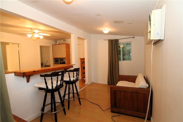 interior space with light brown cabinetry, a breakfast bar, ceiling fan, an AC wall unit, and light hardwood / wood-style floors