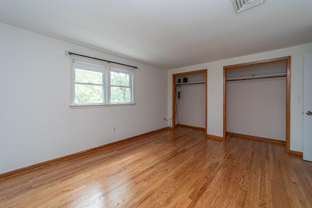 unfurnished bedroom featuring light hardwood / wood-style floors and two closets