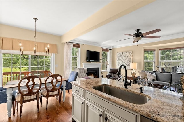 kitchen with light stone countertops, dark hardwood / wood-style flooring, ceiling fan with notable chandelier, sink, and hanging light fixtures