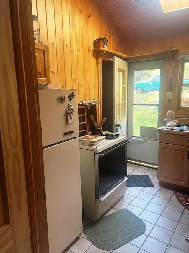 kitchen with wooden ceiling, stove, white fridge, wooden walls, and light tile patterned floors