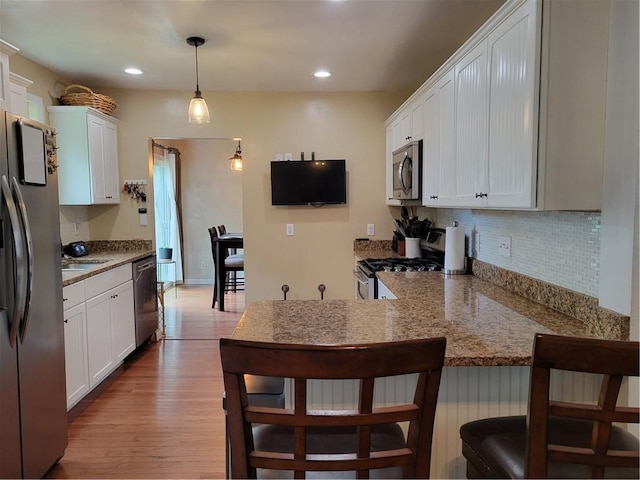 kitchen featuring kitchen peninsula, appliances with stainless steel finishes, pendant lighting, light hardwood / wood-style flooring, and white cabinetry