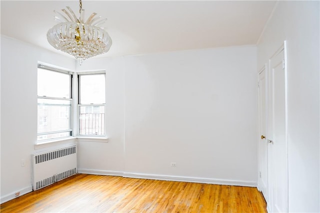 unfurnished room featuring plenty of natural light, light hardwood / wood-style floors, radiator, and an inviting chandelier