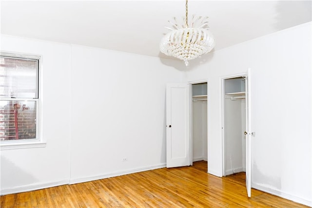 unfurnished bedroom with light wood-type flooring, two closets, and an inviting chandelier