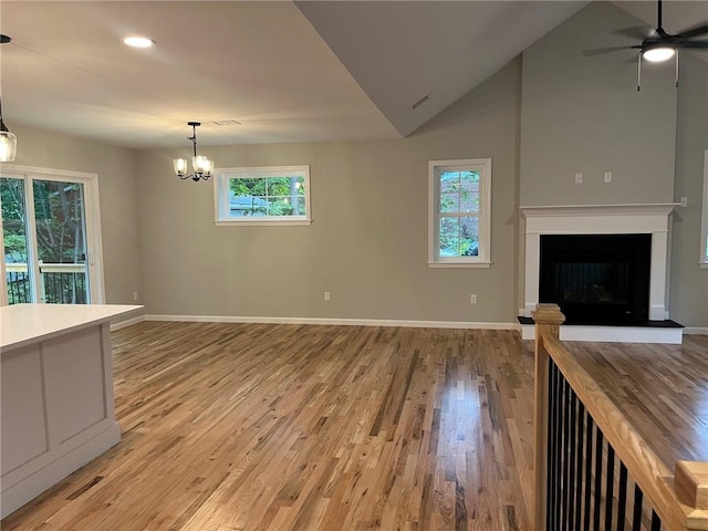 unfurnished living room with ceiling fan with notable chandelier, high vaulted ceiling, and light hardwood / wood-style flooring