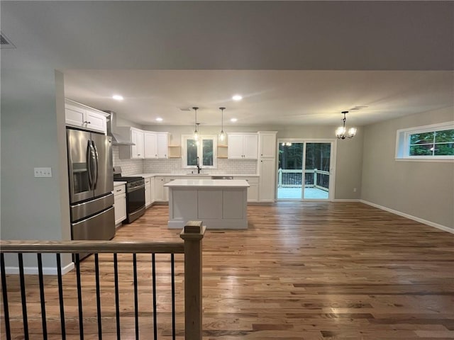 kitchen featuring white cabinetry, black stove, wall chimney exhaust hood, sink, and stainless steel fridge