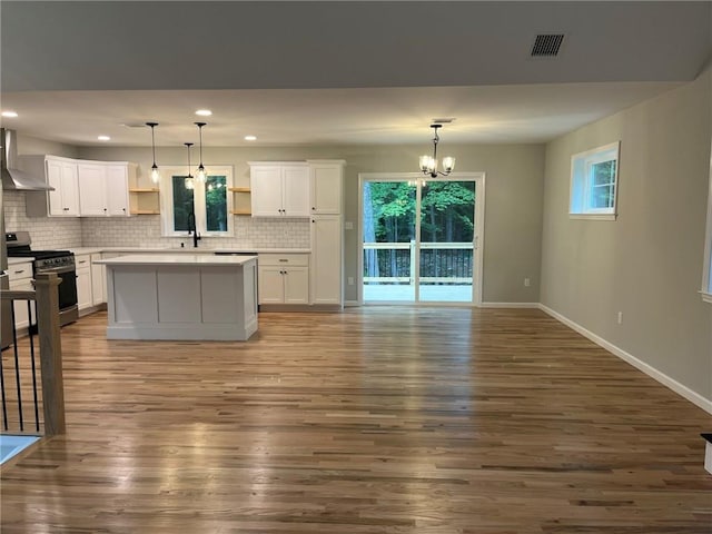 kitchen featuring white cabinets, wood-type flooring, wall chimney exhaust hood, and stainless steel gas range