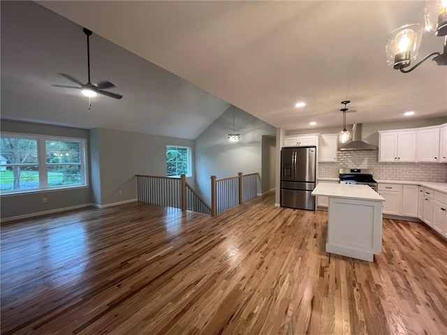 kitchen featuring wall chimney range hood, plenty of natural light, light hardwood / wood-style floors, white cabinets, and appliances with stainless steel finishes