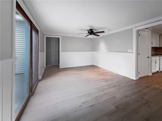 empty room featuring ceiling fan, light wood-type flooring, ornamental molding, and a baseboard heating unit
