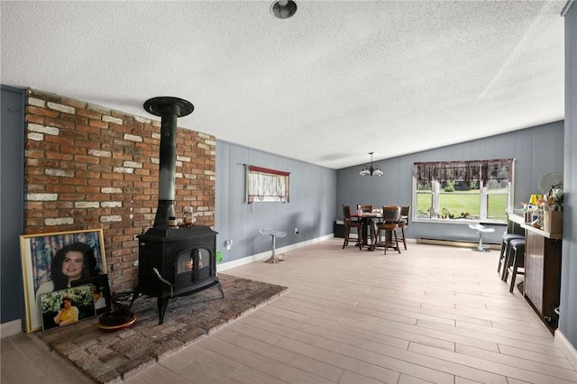 living room featuring a textured ceiling, light hardwood / wood-style flooring, a wood stove, and vaulted ceiling