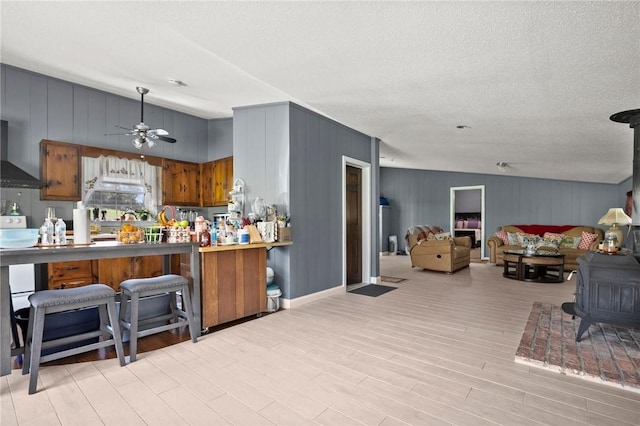 kitchen featuring a wood stove, light hardwood / wood-style flooring, lofted ceiling, and wall chimney range hood