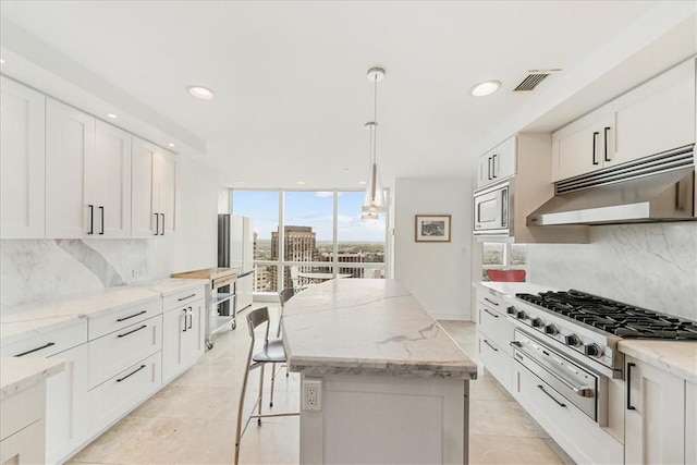 kitchen with white cabinets, decorative backsplash, appliances with stainless steel finishes, decorative light fixtures, and a kitchen island