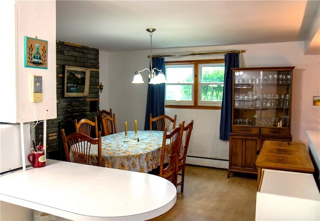 dining space featuring hardwood / wood-style floors, a notable chandelier, a stone fireplace, and a baseboard radiator