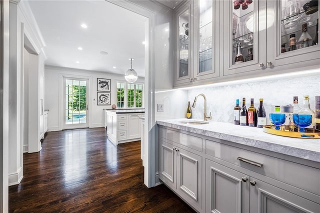 bar with dark hardwood / wood-style flooring, light stone counters, ornamental molding, sink, and white cabinetry