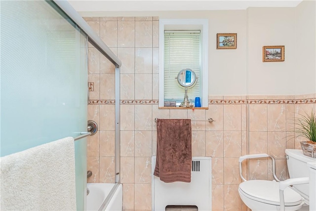 bathroom with radiator, toilet, tile walls, and bath / shower combo with glass door