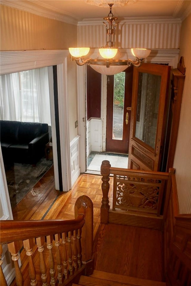 stairs with an inviting chandelier, parquet floors, and crown molding