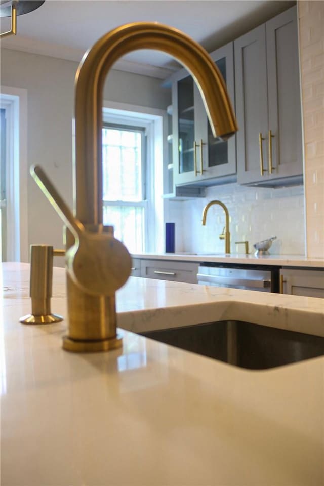 kitchen featuring tasteful backsplash, gray cabinetry, light stone countertops, and dishwasher