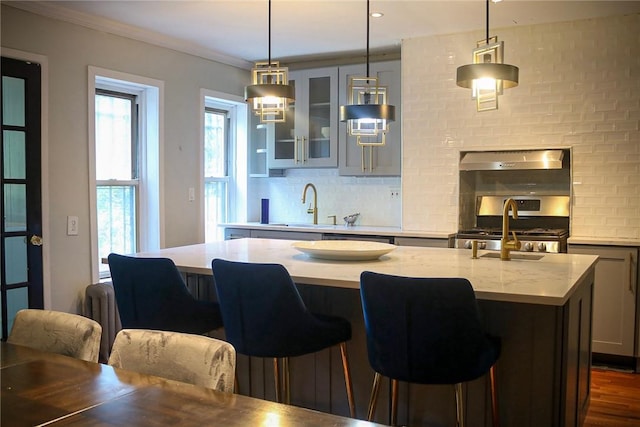 kitchen featuring a breakfast bar, exhaust hood, gas range, an island with sink, and decorative light fixtures